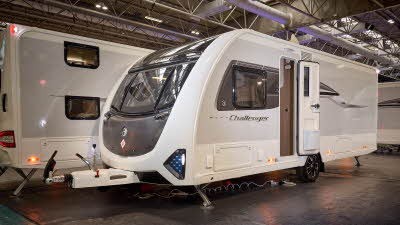 Swift Challenger 580 is white with grey sides and a black front panel.  There are turquoise triangular panels at the front.  Its corner steadies are down and its entrance door is open.