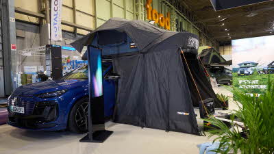 TentBox Lite XL has blue and black canvas.  It has an extension.  It is shown on a blue Audi.  There is an interactive stand next to it.
