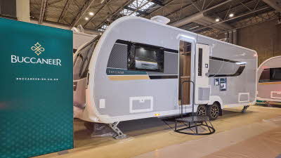 Buccaneer Skylinder Commodore has a grey exterior with a black decal with a teal and yellow strip under the window.  The entrance door is open and there is a black metal step to gain easy access to the interior.