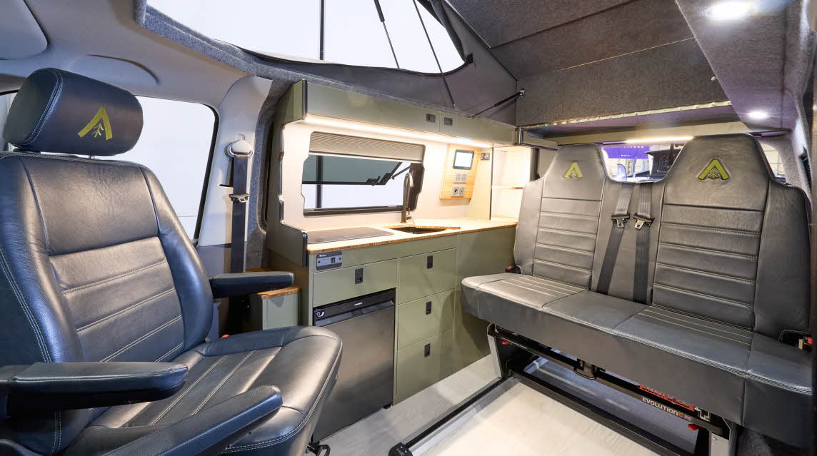 Wildtracks Campervans Explorer has a cream floor with black leather upholstery. The cabinets are green. The rising roof is open.
