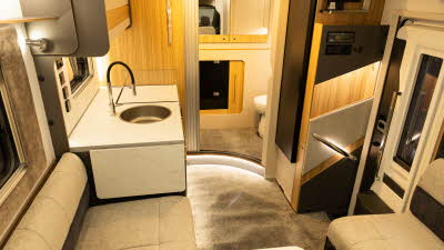 The Bailey Adamo 69-4 has cream and brown upholstery.  The kitchen is in the centre with a round sink and a work top extension flap is next to the sofa.  The washroom is at the rear and its Tambour door is open.