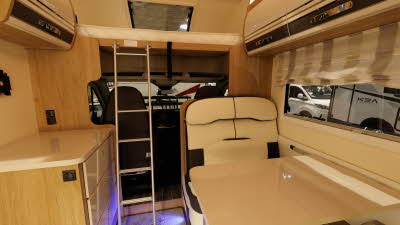 The Roller Team Auto-Roller 746 has cream and brown upholstery.  The sofas are positioned around a table.  To the left there is a ladder for access to the roof bed.