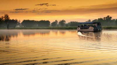 A boat on the calm waters  of Yellow Water Billabong under an amazing golden sky in Kakadu National Park Australia