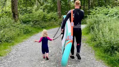 Walking down a track an adult carrying a paddleboard and child walking beside him 