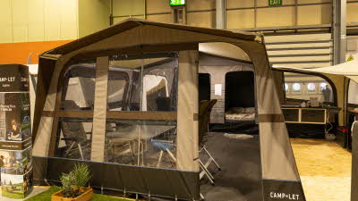 The Camp-Let Earth has coffee and cream coloured canvas.  The dining table with four chairs is at the front, to the rear the bedroom doors are open.  There is an annex with the kitchen set up.