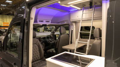 The Bespoke Leisure Bespoke Zermatt Edition has black upholstery.  There is a hob by the open door.  There is a ladder for easy access to the roof bed and there is purple accent lighting.