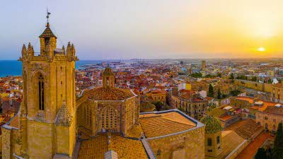 An aerial of Primatial Cathedral of Tarragona and the sandy-coloured buildings under a beautiful sunset sky in Catalonia, Spain. This is the final destination on our suggested route from Calais