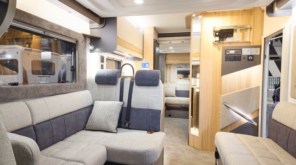 The Bailey Adamo XL DL has beige carpets, with cream and pale wood cabinets.  The upholstery is cream and dark brown.  There is another lounge to the rear.  