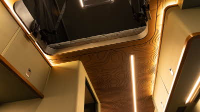 The Knights Custom Conversions Prestige XL has a wooden ceiling with a pattern, the cabinets are green with wooden edging.  The open pop top roof has an fan unit for air circulation.