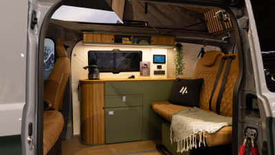 The Maverick Outdoors Expedition has tan upholstery with green and wooden cabinets.  Its rising roof is open.