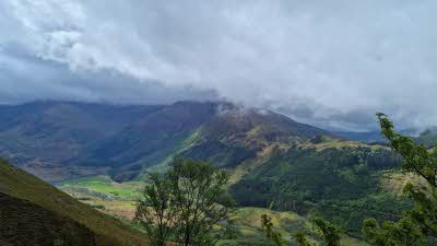 A view from part way up Ben Nevis looking out over the shades of green on the surrounding slopes under a mystical cloudy sky