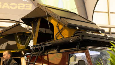 The Escapade 4x4 Horizon has orange and black canvas and a dark hard shell roof.  There is a black ladder to gain access.  It is shown on a dark red 4x4.