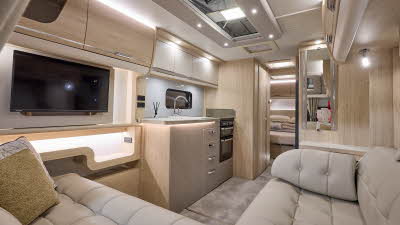 Interior of the Elddis Crusader Borealis with cream leather sofas, cosy cushions, wood accents and beige carpets.  The door to the rear bedroom is open.  Perfect for relaxation and designed for comfort.