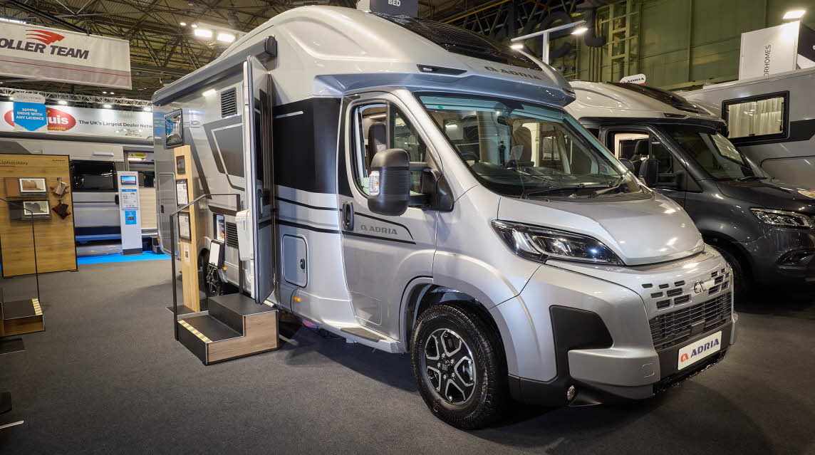 The Adria Matrix Supreme has a silver exterior.  The habitation door is open and there are two steps to gain easy access. There is an information board to the left of the steps.  