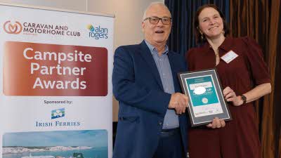 A Caravan and Motorhome Overseas Campsites Award Runner Up with the Chairman next to a sign showing Campsite Partner Awards, with Irish Ferries below it