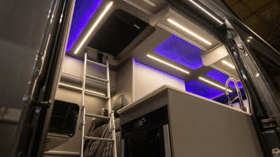 The Bespoke Leisure Bespoke Zermatt Edition has black upholstery.  There is a hob by the open door.  There is a ladder for easy access to the roof bed and there is purple accent lighting.
