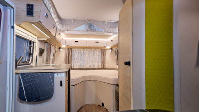 Eriba Touring 542 Urban Nugget Gold interior, it is white and cream with a yellow vertical panel.  There is a dinette at the front.  The fixed bed is beyond the kitchen.  