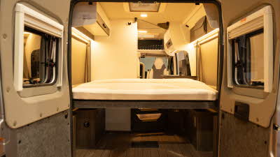 The VANTourer 540 D has a rear bed with a large storage area underneath.  Its rear exterior doors are open.