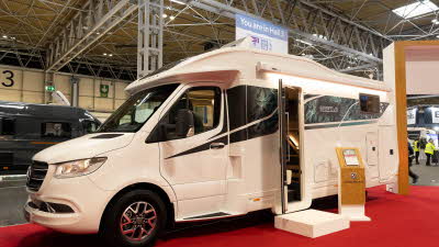 The Coachman Sportivo 565 is white with black and green patterned decals.  Its habitation door and skylights are open.  There is a step beside the habitation door to gain easy access.  There is an information close by.