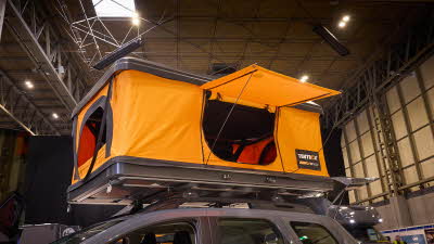 TentBox Classic 2.0 has orange canvas and a hard top and base.  Its door is open.  It is shown on the roof rack of a vehicle.