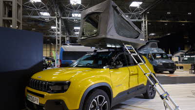 The TentBox GO is shown on a yellow jeep.  Its canvas is grey with black windows.  There is a silver ladder.