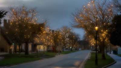 View of a road through the village with houses on either side. Trees with golden lights line the road, with old style street lamps alongside