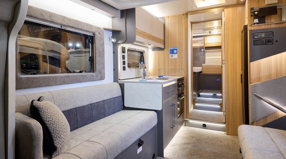 The Bailey Adamo XL T has beige carpets, with cream and pale wood cabinets.  The upholstery is cream and dark brown.  There are three steps up to the fixed rear bed.  