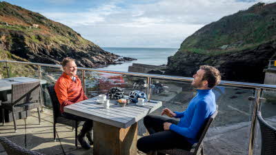 Two men in cycling gear eating breakfast with stunning coastal view in the background