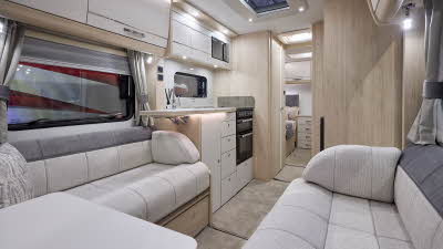 Interior of the Elddis Crusader Shamal with two tone grey sofas, cosy cushions, wood accents and beige carpets.  The door to the rear bedroom is open.  Perfect for relaxation and designed for comfort.