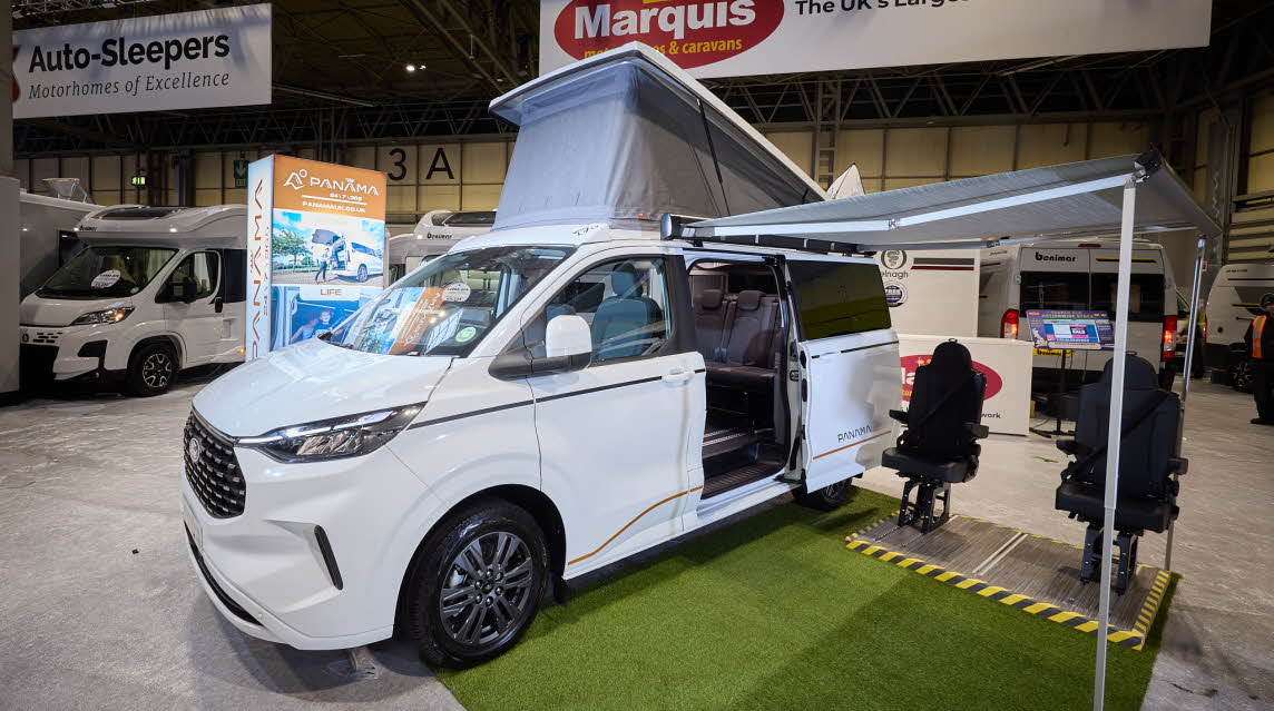 The Panama P-12 is white and has a grey rising roof which is fully extended.  There is a large canopy awning with two black chairs and there's Astroturf on the floor.