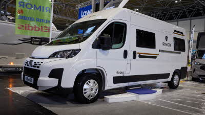 The Rimor Horus 40 is white with gold decals and black trim.  There are white steps by the closed sliding habitation door.  Its skylight is open.