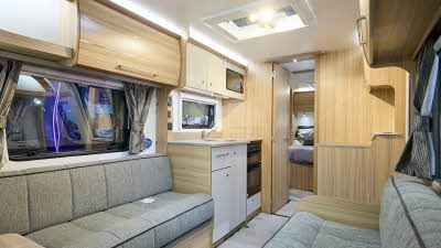 Bailey Phoenix GT75 640’s interior has pale wooden furniture with grey upholstery.  The kitchen is in the middle with a bedroom with a fixed island bed to the rear.  There is a roof light above the kitchen.