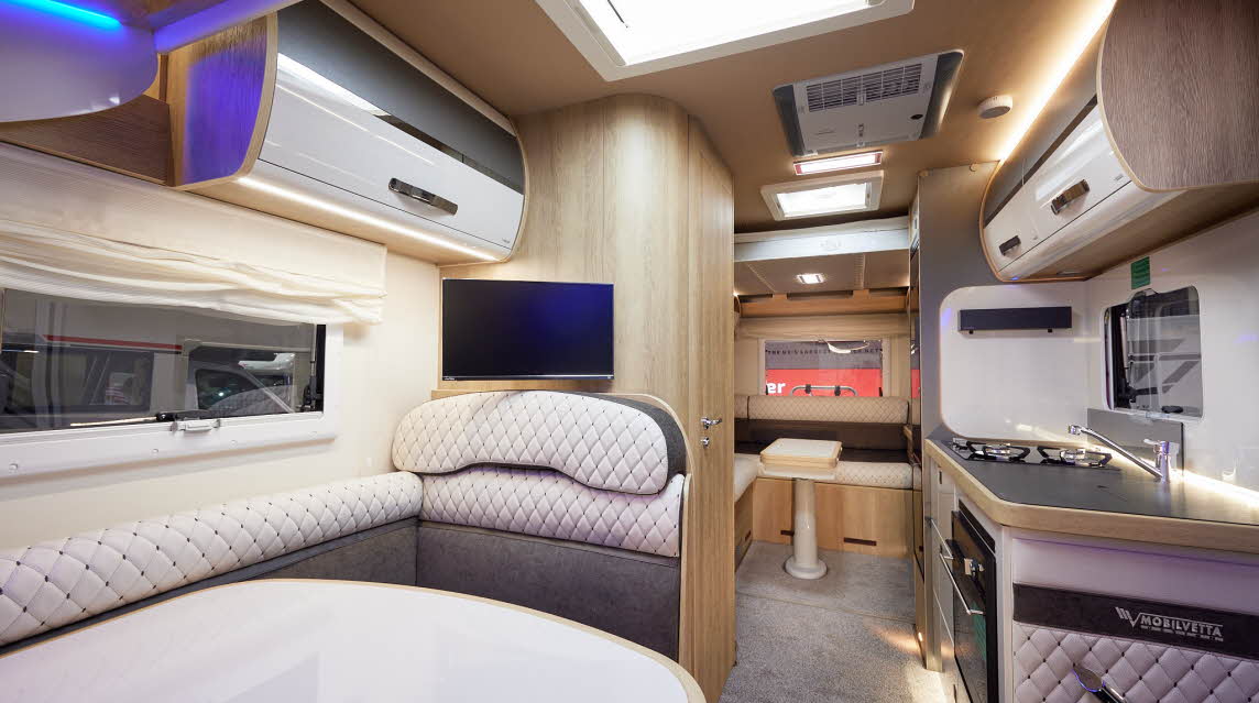 Mobilvetta Tekno Line K-Yacht 80 has two tone grey and cream embossed upholstery.  There are two tone overhead lockers. The floor has a grey carpet.  Towards the rear of the vehicle there is a rear lounge.