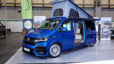 Ecowagon Expo+ exterior the campervan is royal blue and the sliding door is open showing into the interior, the rising roof is fully open showing grey canvas and three windows.