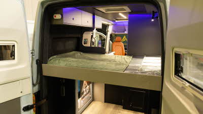 The AURA 6EB's rear doors are open revealing its rear bed.  There are overhead cabinets at the rear of the bed.