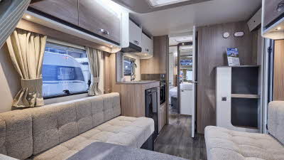 Interior of the Swift Sprite Major 4 EB with beige sofas, wood accents and a wooden floor.  The large roof light will let natural light flood in.  The mid washroom door is open as is the door to the bedroom.