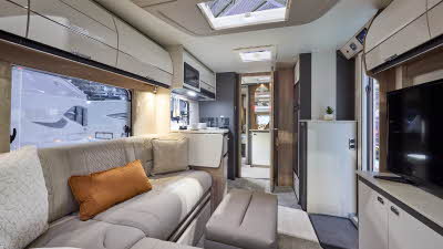 Interior of the Swift Swift Elegance Grande 850 with leather sofas, cosy cushions and pale carpets.  There is a leather pouffe for comfort.  The large windows and four sky lights will let natural light flood in.  The door to the mid washroom is open.
