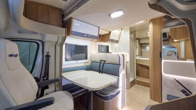 The Elnagh Baron 579 has a wooden floor and white and grey cabinets.  The upholstery is cream with grey seating and blue backrest.  There is a step to the rear fixed bed.