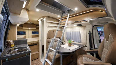 Malibu Van diversity GT skyview 600’s interior has beige and brown leather upholstery.  One rear seat has a fitted seat belt.  There is a silver ladder next to the table for access to the roof bed.  To the rear there is a fixed bed.