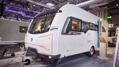 The Coachman VIP 520 has a white exterior with a brown patterned decal.  Its sunroof is open.  The entrance door is open and there are two wooden steps to gain easy access.  There is a stand next to the steps.