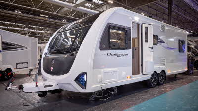 Swift Challenger Grande 630 is white with grey sides and a black front panel.  There are turquoise triangular panels at the front.  Its corner steadies are down and its entrance door is open.