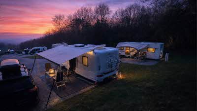 Lickpenny Matlock Club Campsite looking onto pitched caravans as the night falls with dark trees along the edge under a stunning pink, purple and orange sky as the sun sets. 