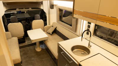 The Bailey Adamo 69-4 has cream and brown upholstery.  There is a white extendable table in the centre of the lounge.  The kitchen is in the bottom right with a round sink.