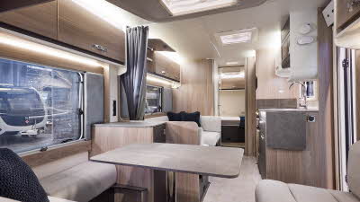 Interior of the Swift Challenger Grande 630 with beige sofas, cosy cushions and beige carpets.  The large windows and three sky lights will let natural light flood in.  The dinette is opposite the kitchen.