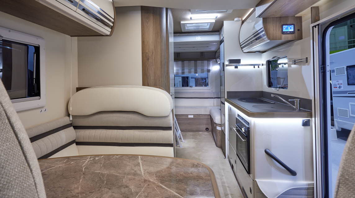 Roller Team T-Line 700 has white and brown upholstery with matching overhead lockers.  The carpet is cream.  There is a large marble effect table.  Towards the rear there is a rear lounge.  