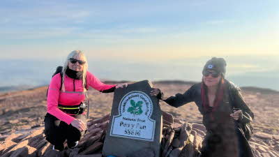 two happy walkers pose by the marker at the top of Pen-y-Fan