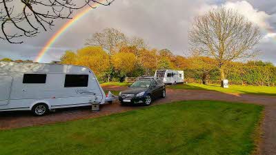 Caravan and tow car parked in field with rainbow in the sky