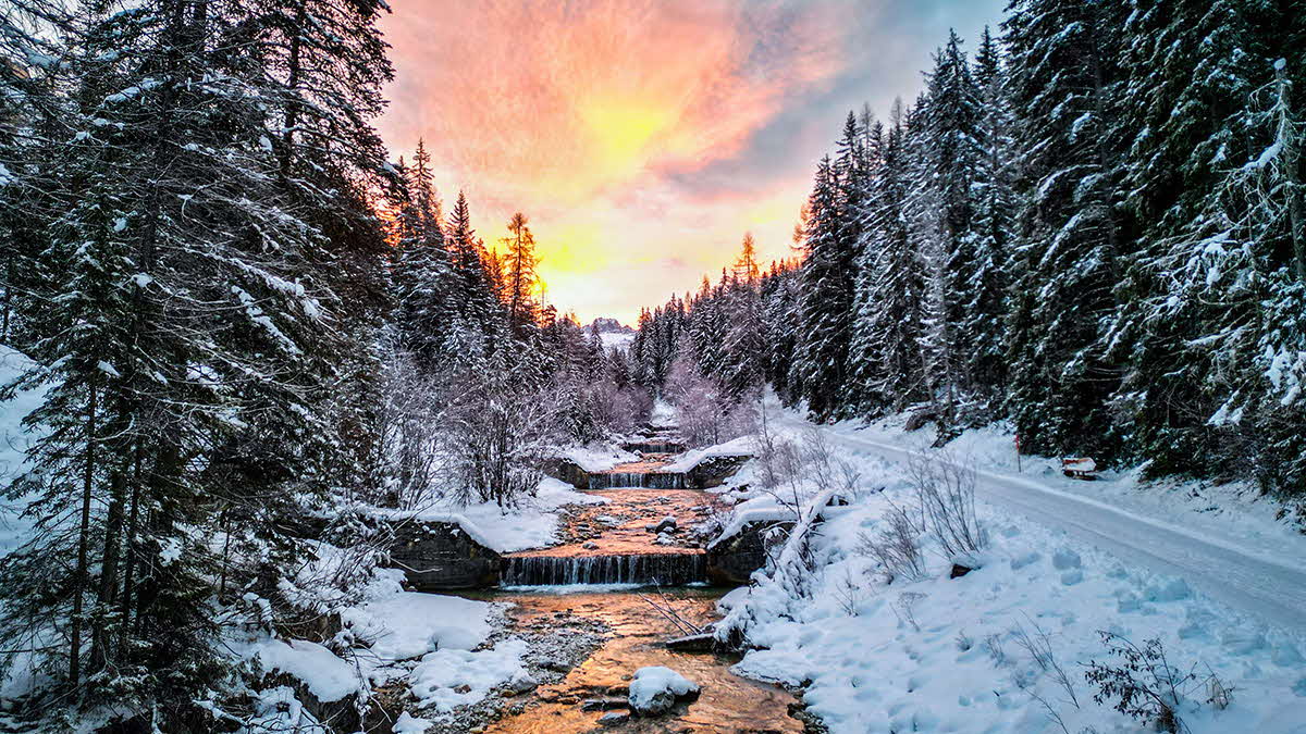 Sunset over a snowy scene with a frozen stream in the Dolomites. 
