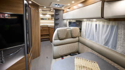 Carthago c-tourer I 145 RB LE superior’s interior has beige leather upholstery with fabric panels.  The furniture is wooden with cream doors.  Nets curtains hang at the windows.  There are two fixed beds to the rear.  