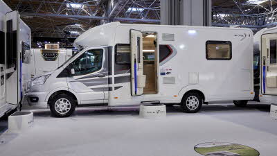 Auto-Trail F-Line F74 exterior, the motorhome is white with grey decals on the side, the habitation door is open showing into the interior, with a step to gain easy access.  There is a blue Auto-Trail umbrella in the door.